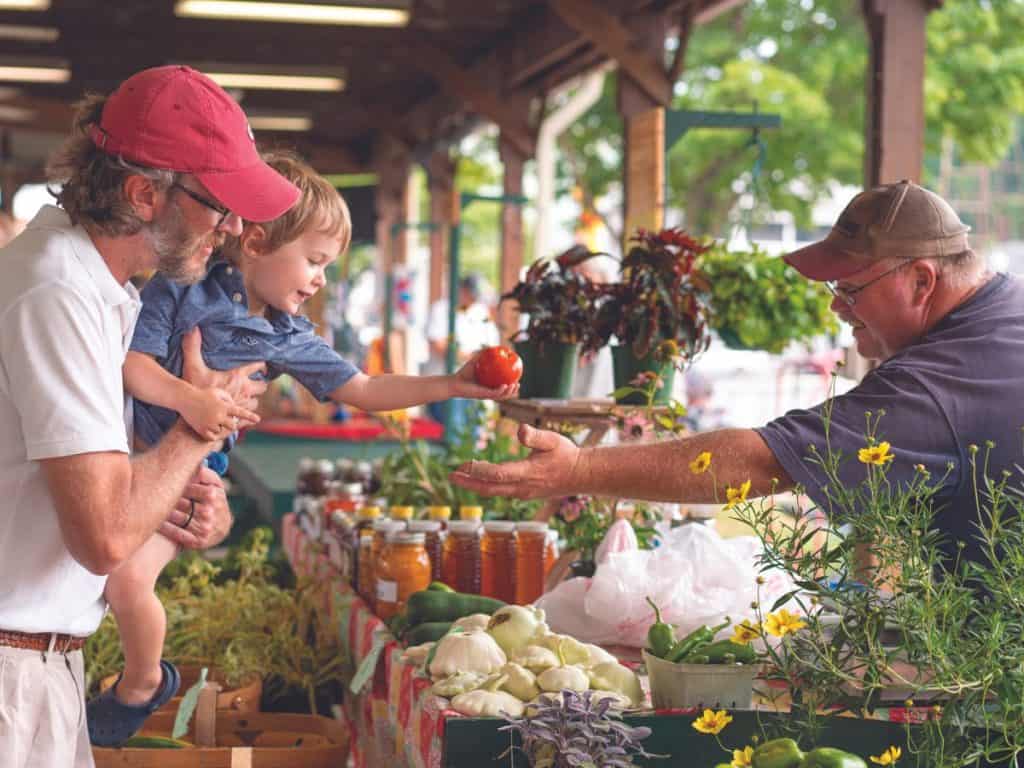 Farmers market vendor hands an apple to a small boy